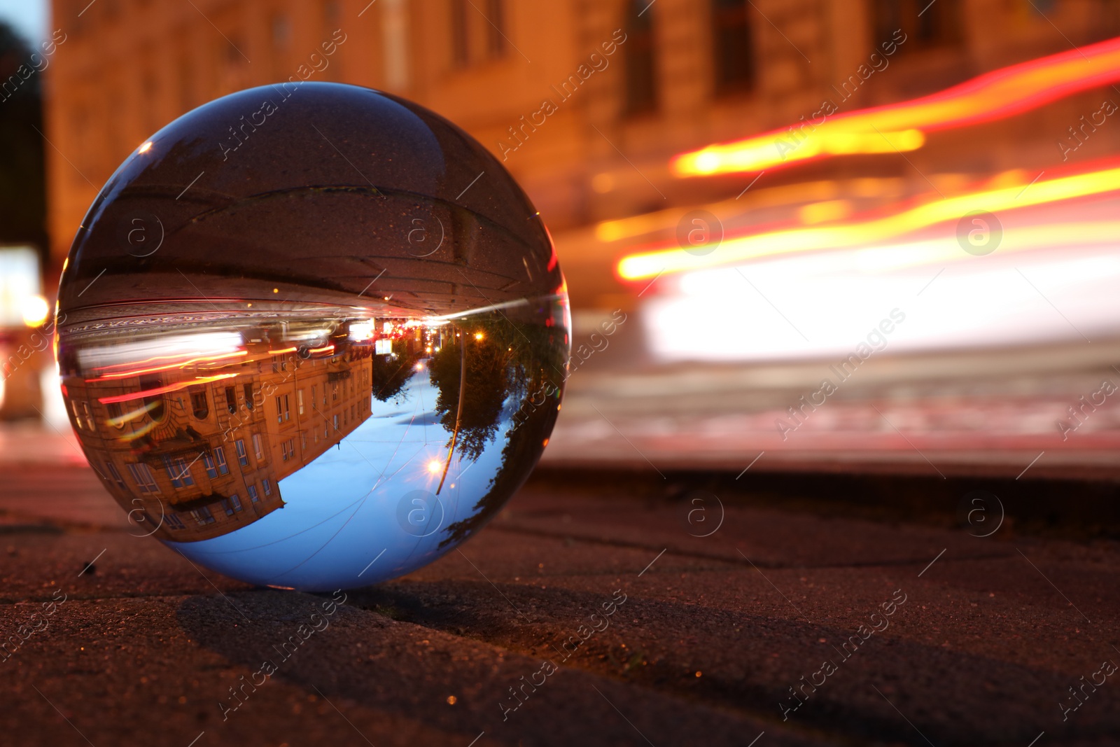 Photo of Beautiful city street, overturned reflection. Crystal ball on asphalt road at night. Space for text