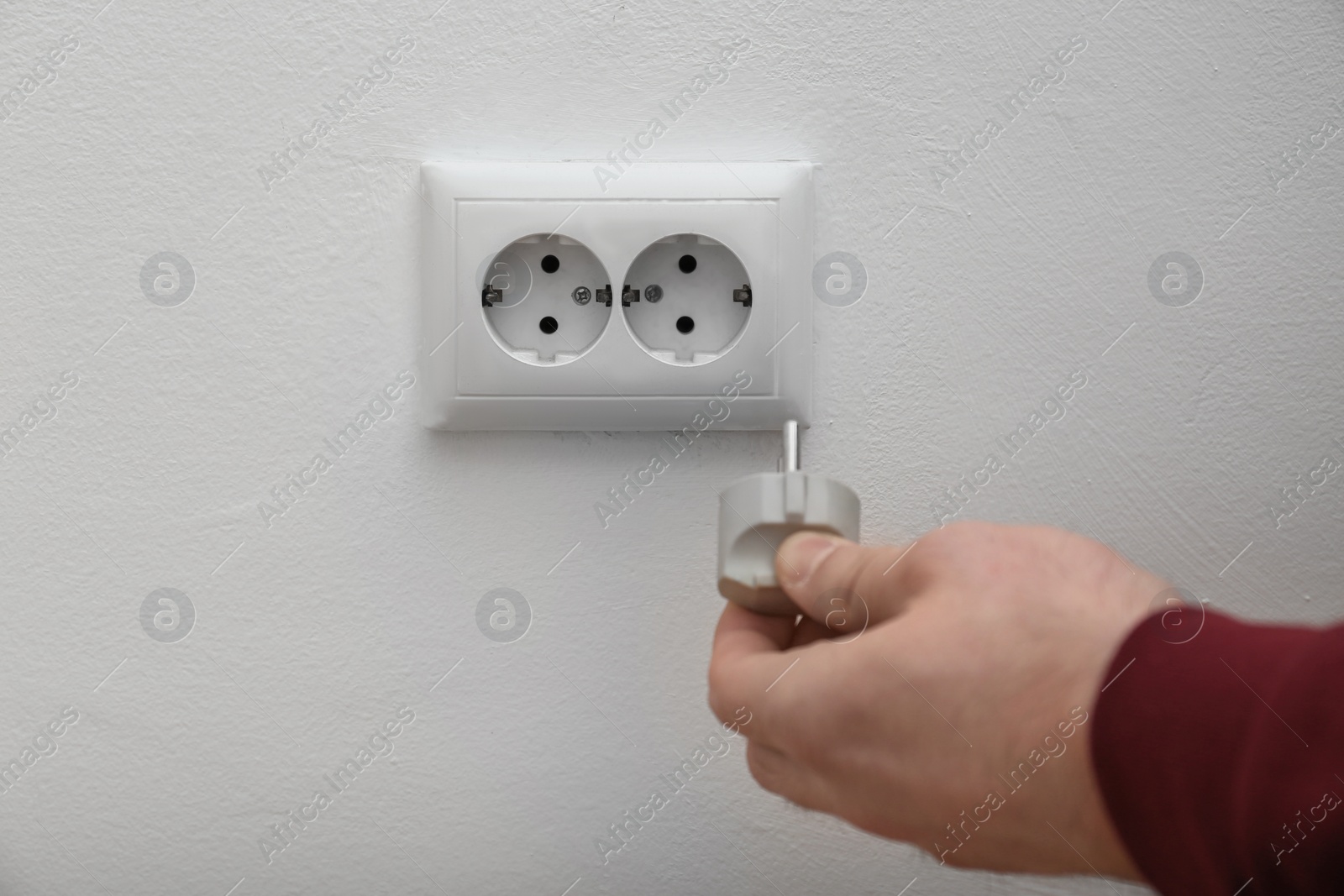 Photo of Electrician inserting plug into power socket on white background, closeup