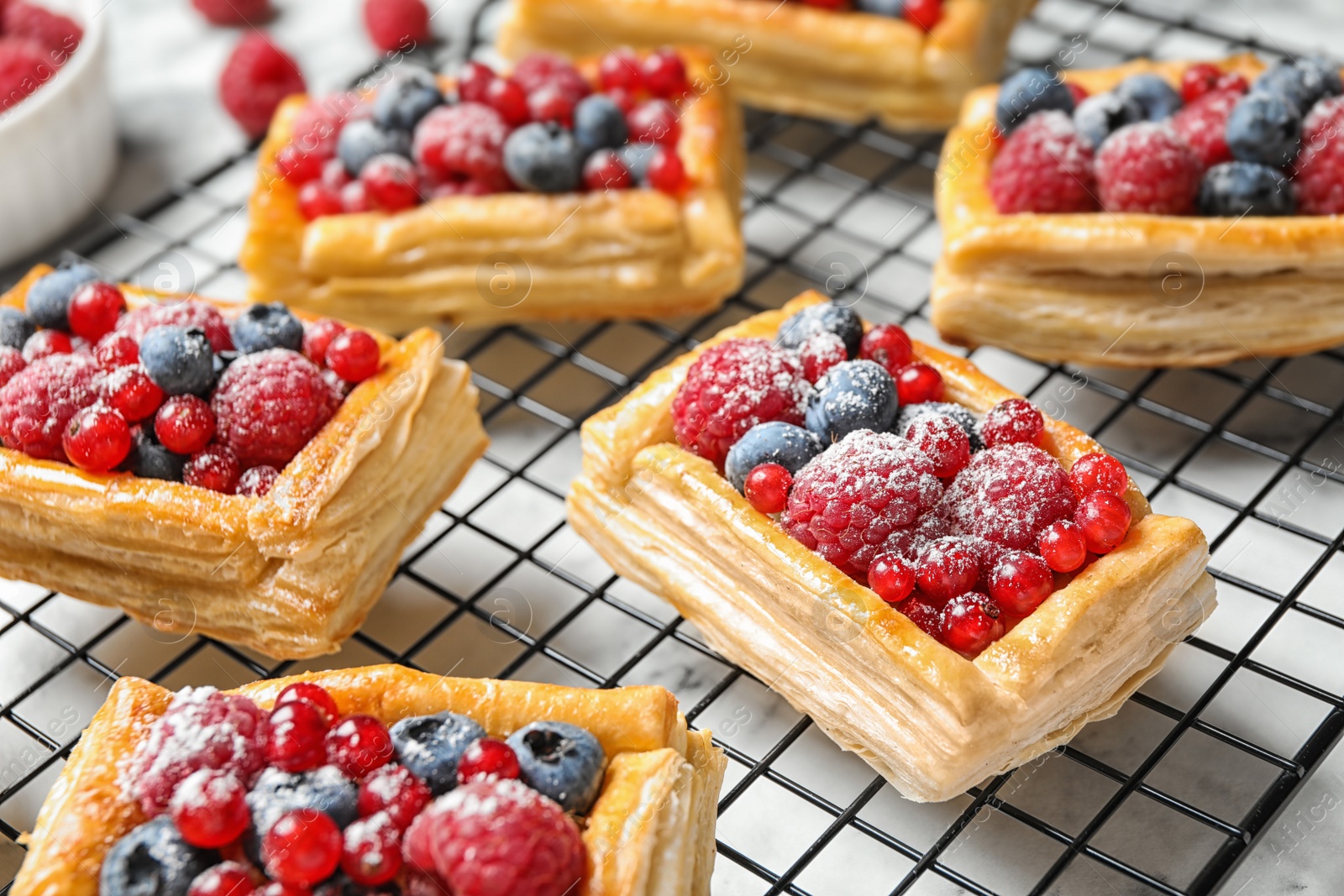 Photo of Cooling rack and fresh delicious puff pastry with sweet berries on white marble table, closeup