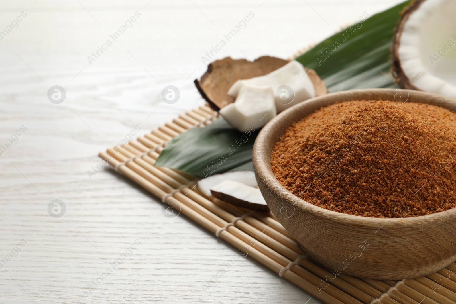 Photo of Natural coconut sugar in bowl on white wooden table, space for text