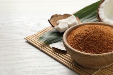 Photo of Natural coconut sugar in bowl on white wooden table, space for text