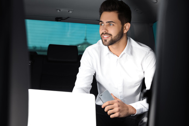 Young man working with laptop on backseat in modern car