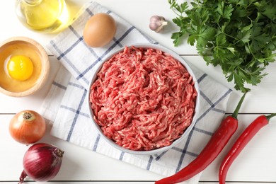 Raw ground meat in bowl and different products on white wooden table, flat lay