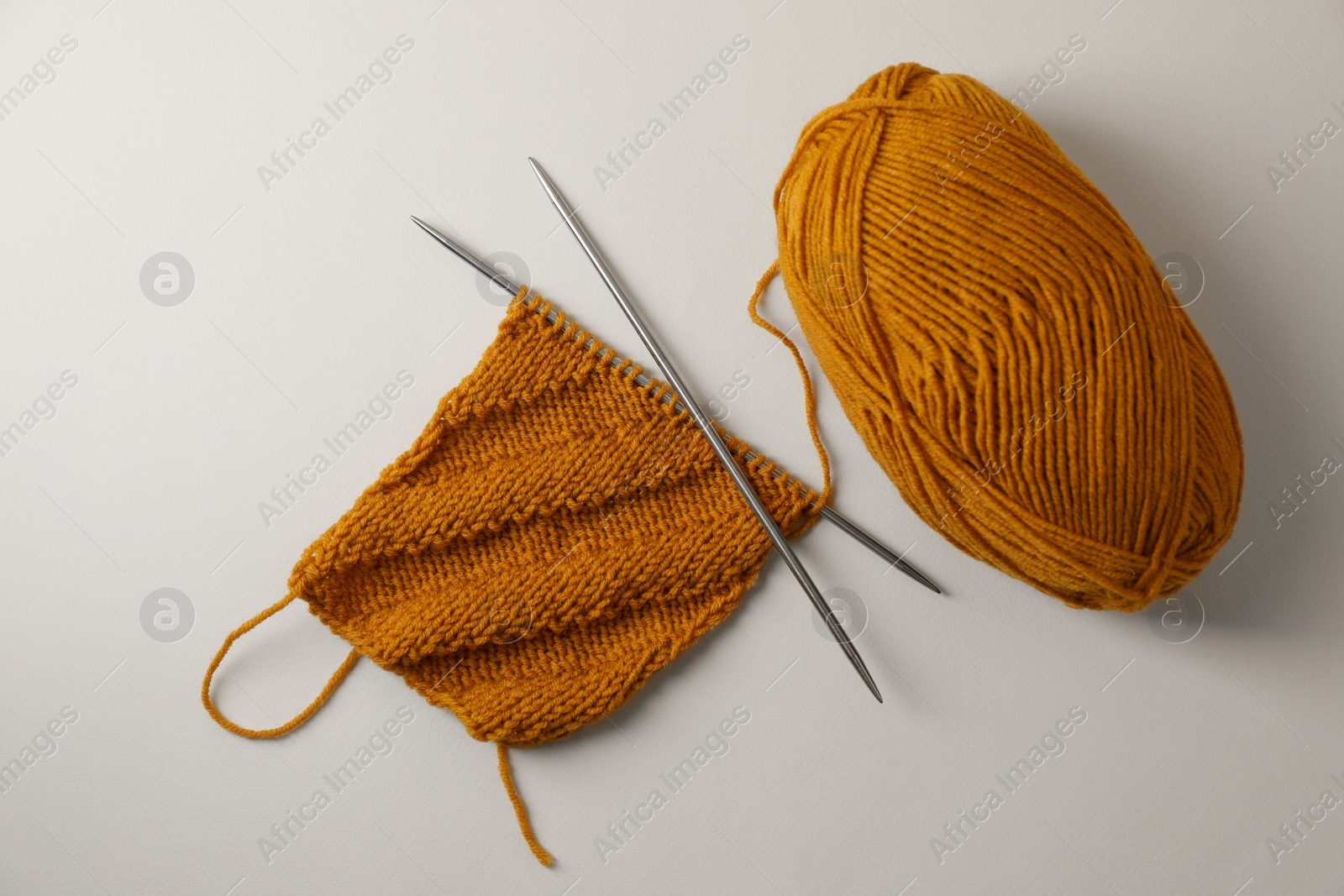 Photo of Soft orange yarn, knitting and metal needles on beige background, flat lay