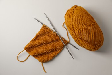 Soft orange yarn, knitting and metal needles on beige background, flat lay