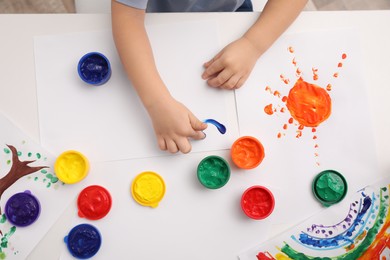Photo of Little child painting with finger at white table indoors, top view