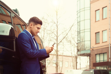 Image of Handsome man with smartphone near modern car outdoors