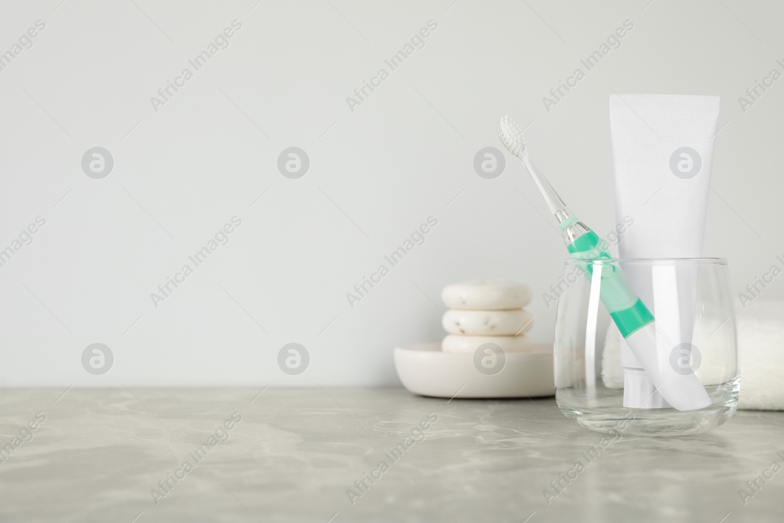 Photo of Electric toothbrush in glass and tube with paste on light grey marble table. Space for text