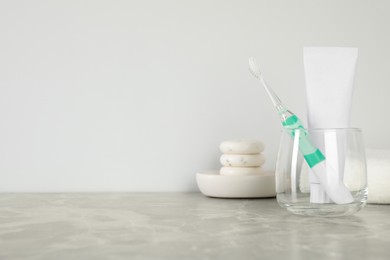 Photo of Electric toothbrush in glass and tube with paste on light grey marble table. Space for text