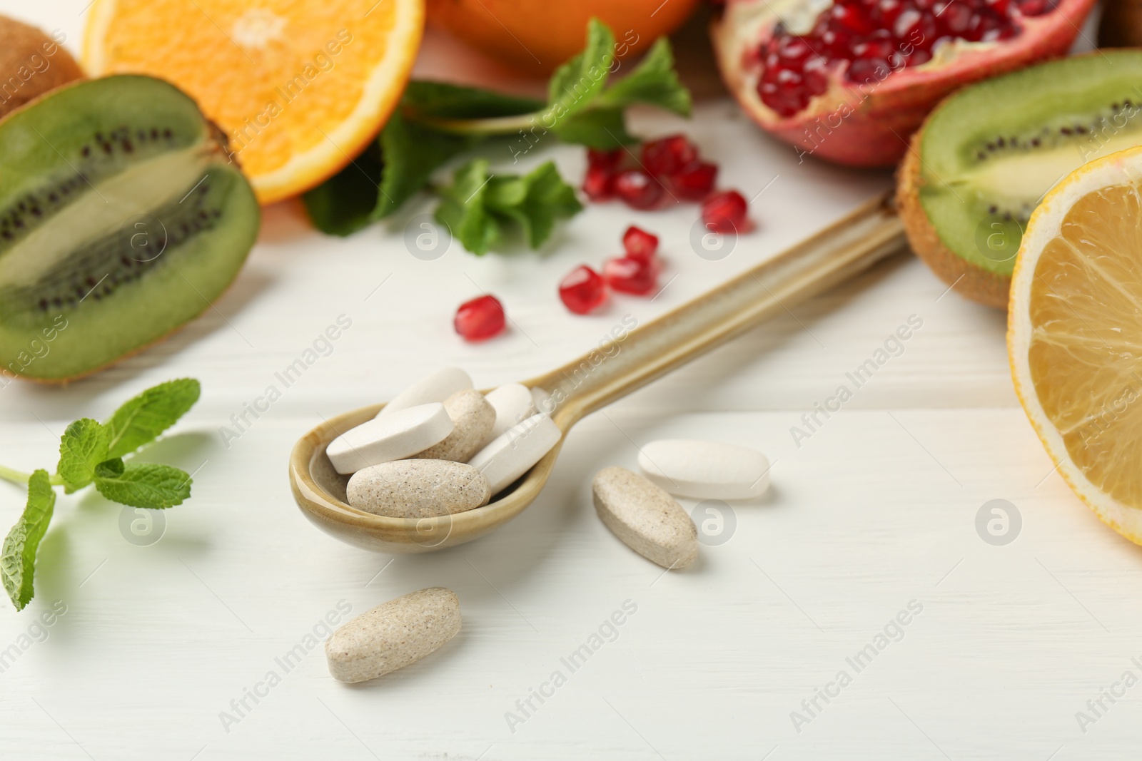 Photo of Different vitamin pills in spoon and fresh fruits on white wooden table