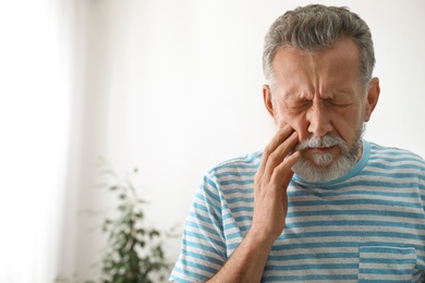 Photo of Mature man suffering from strong tooth pain at home, space for text