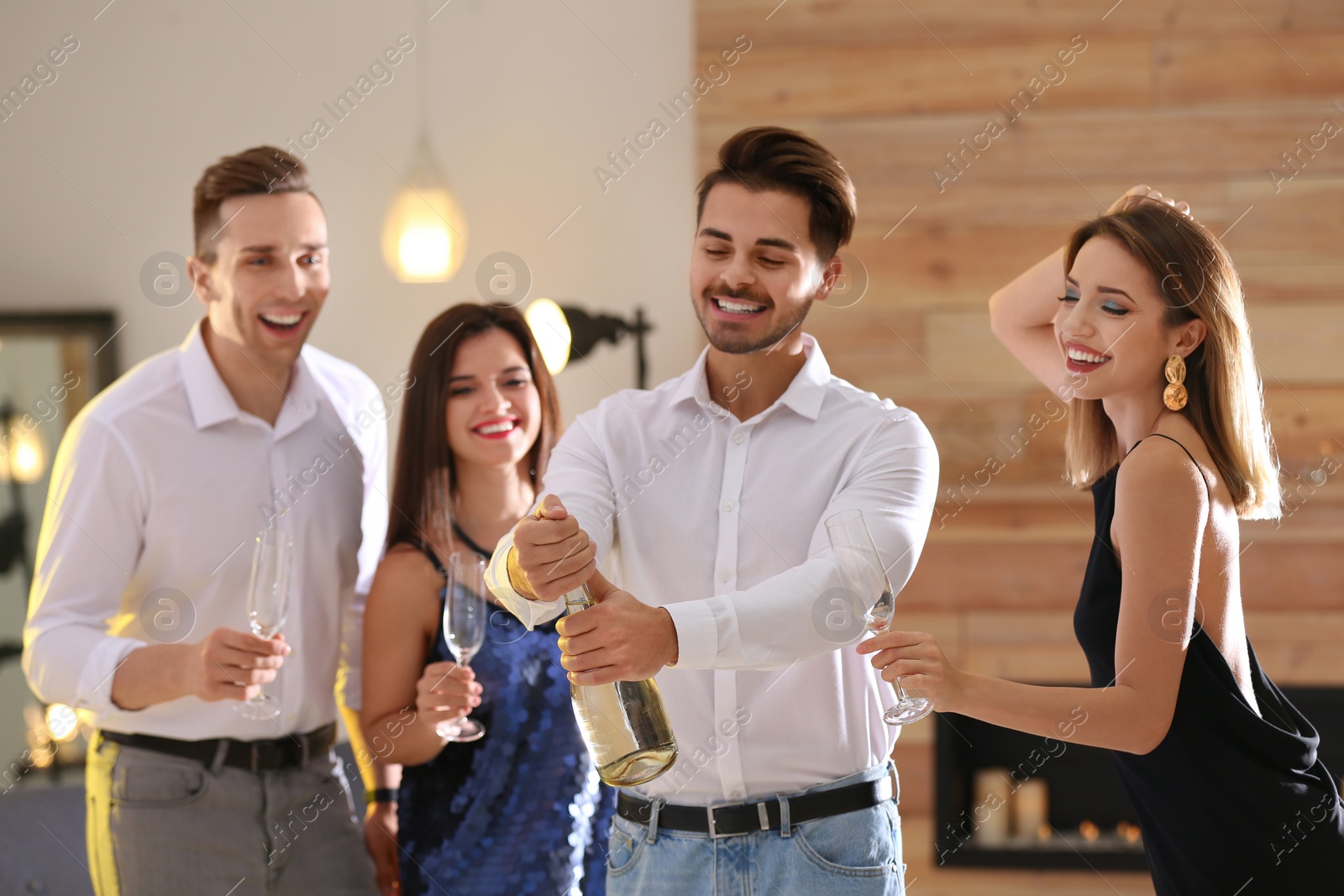 Photo of Man opening bottle of champagne among friends at party indoors