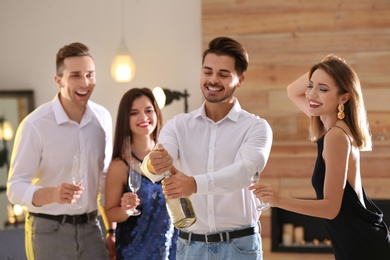 Man opening bottle of champagne among friends at party indoors