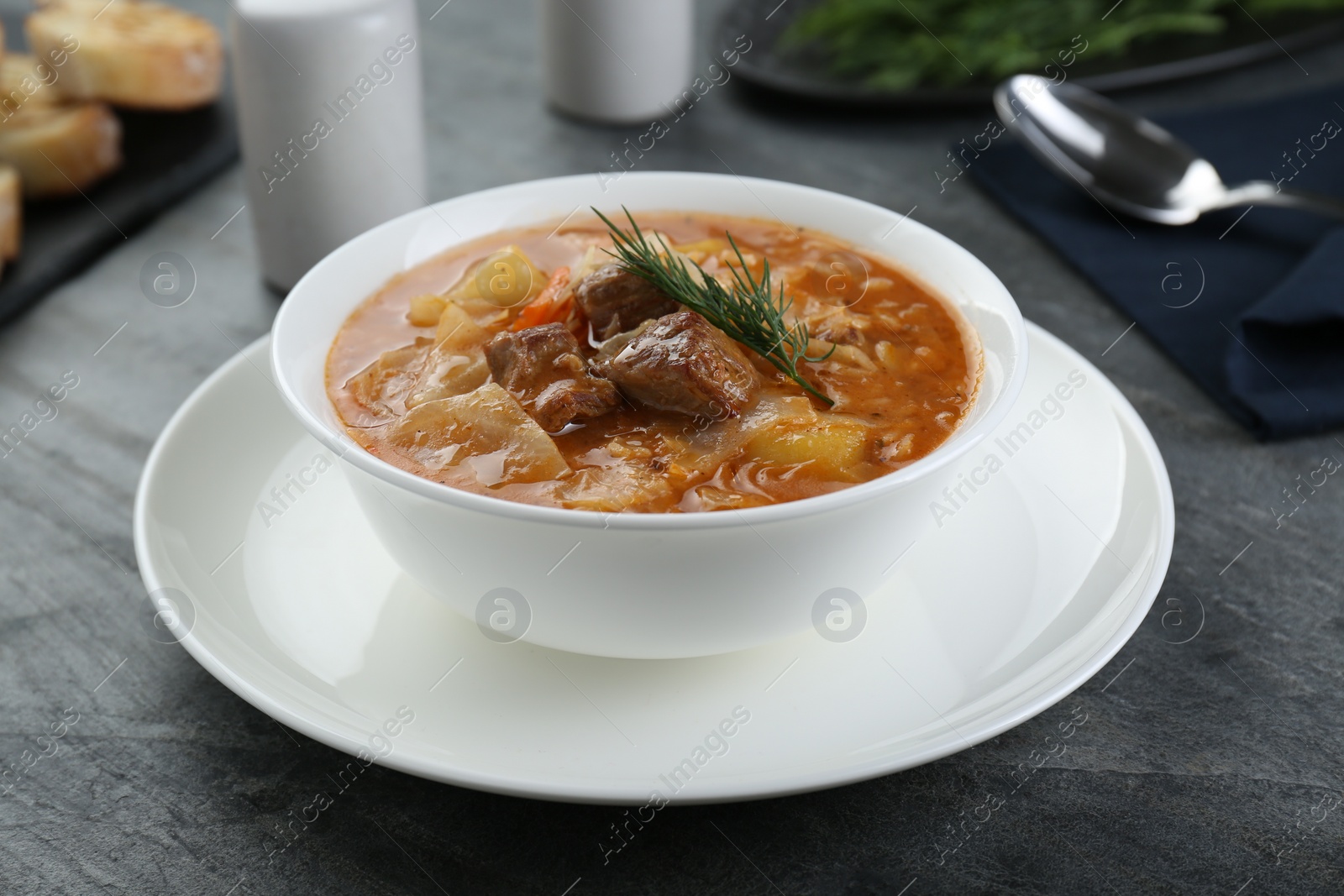 Photo of Tasty cabbage soup with meat, carrot and dill on black table, closeup