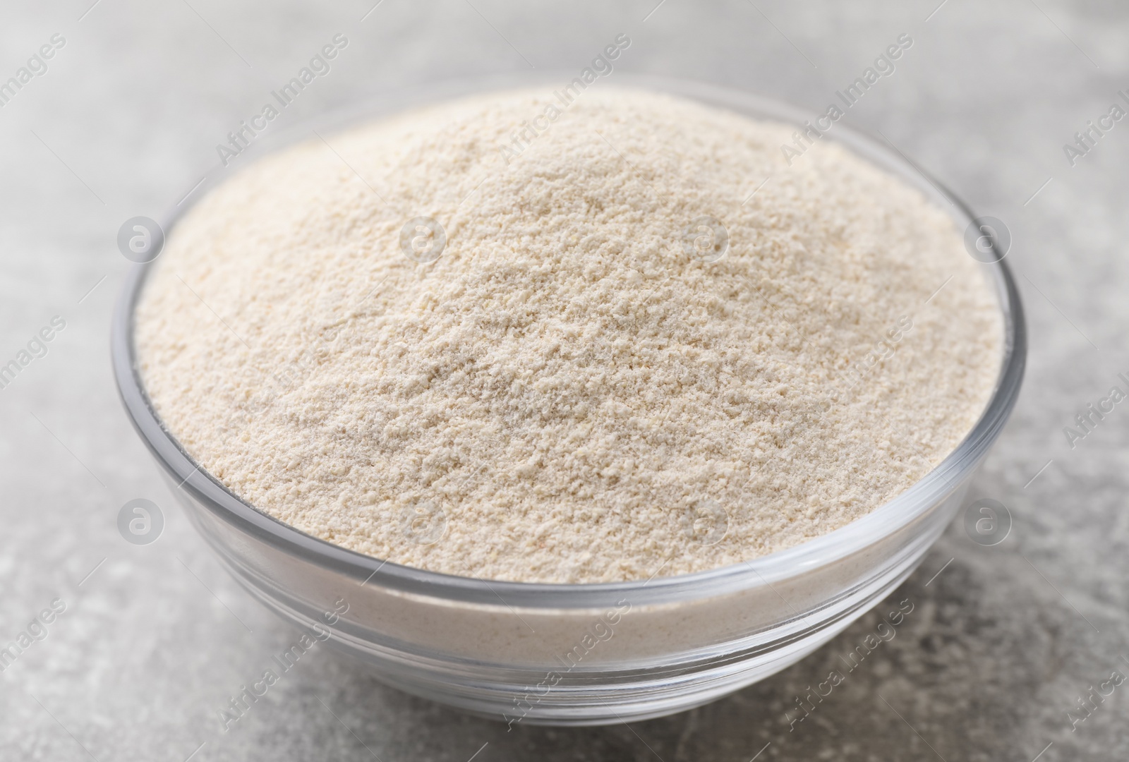 Photo of Glass bowl with quinoa flour on light grey table, closeup