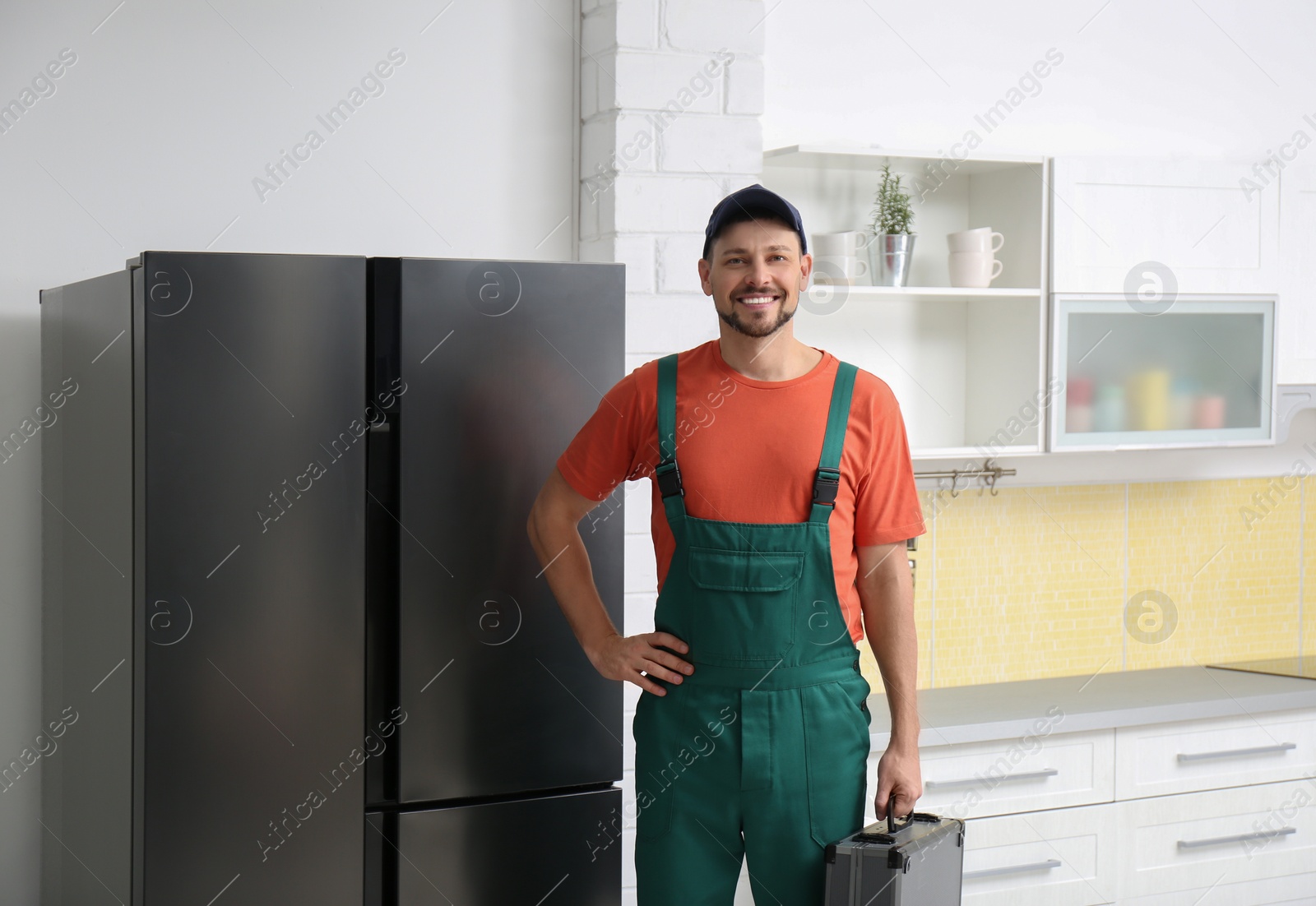 Photo of Male technician with tool box near refrigerator indoors