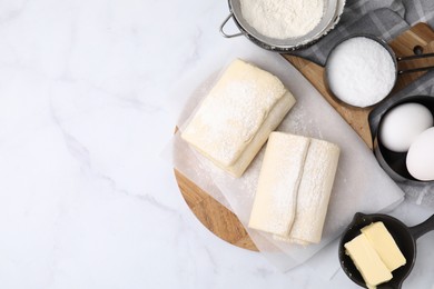 Photo of Raw puff pastry dough and ingredients on white marble table, flat lay. Space for text