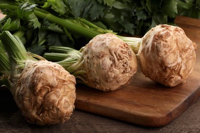 Photo of Fresh raw celery roots and leaves on wooden table, closeup