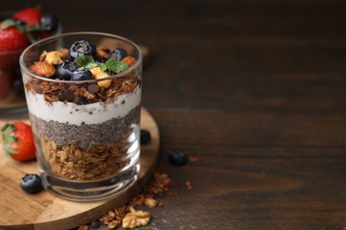 Photo of Tasty granola with berries, nuts, yogurt and chia seeds in glass on wooden table, space for text