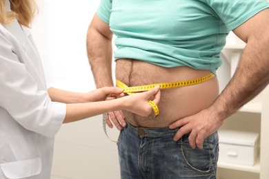 Photo of Doctor measuring overweight man's waist in hospital, closeup