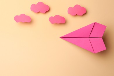 Handmade pink paper plane with clouds on beige background, flat lay. Space for text