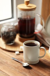 Photo of Cup of freshly brewed tea and spoon with sugar on wooden table, space for text