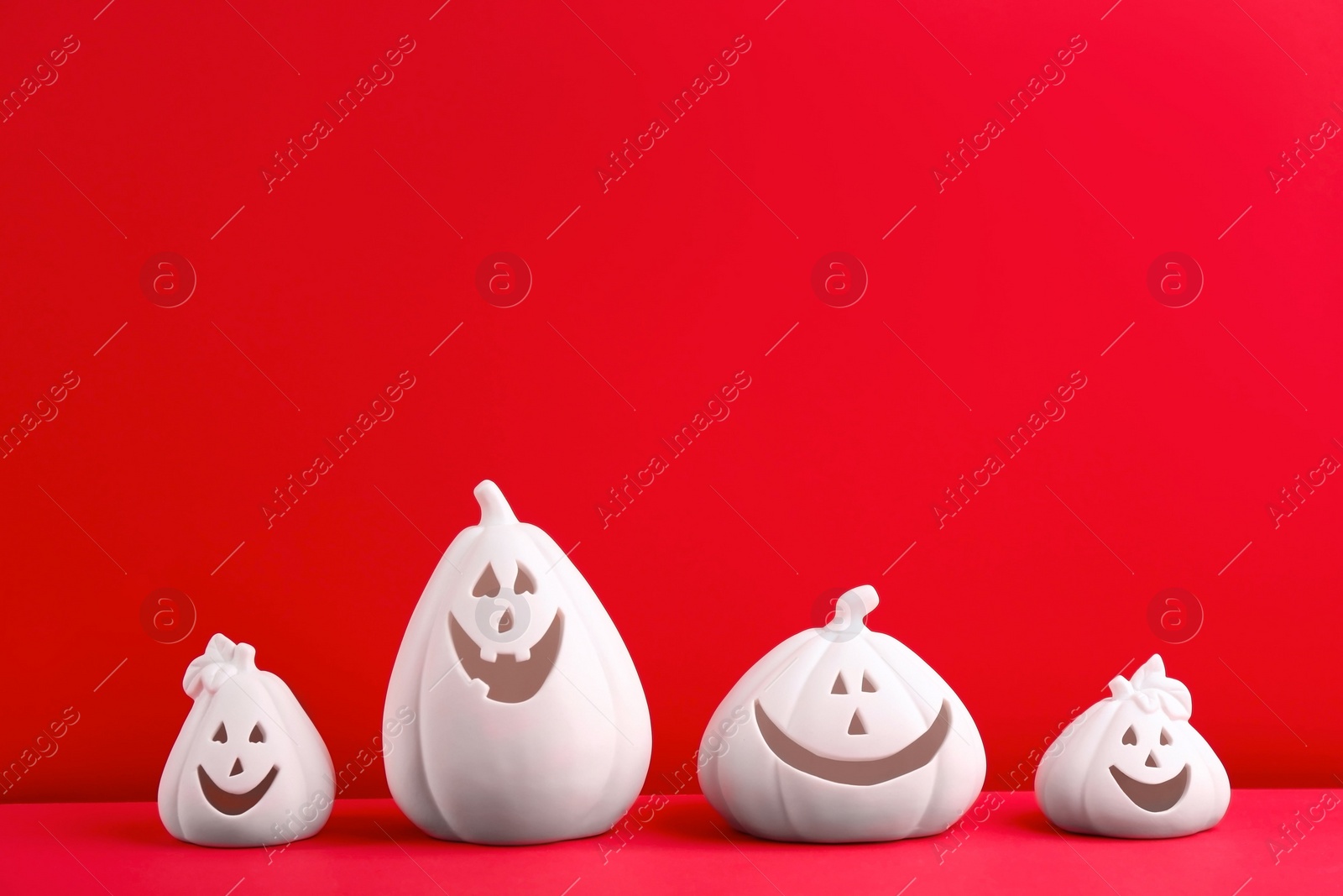 Photo of White pumpkin shaped candle holders on red background, space for text. Halloween decoration