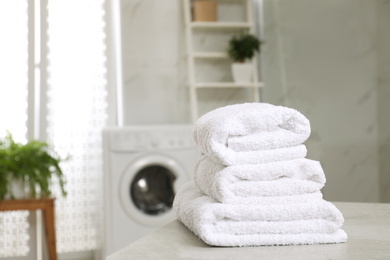 Photo of Stack of clean towels on table in laundry room. Space for text