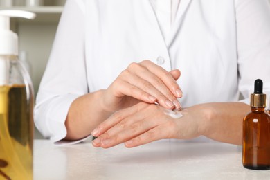 Photo of Dermatologist testing cosmetic product at white table indoors, closeup