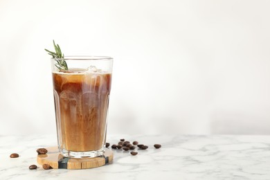 Photo of Refreshing iced coffee with milk and rosemary in glass and beans on white marble table, space for text