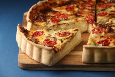 Photo of Cut delicious homemade quiche with prosciutto, tomatoes and greens on blue table, closeup