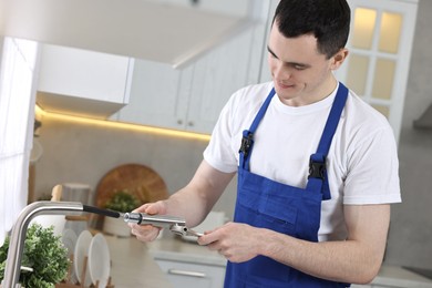 Photo of Young plumber repairing faucet with spanner in kitchen