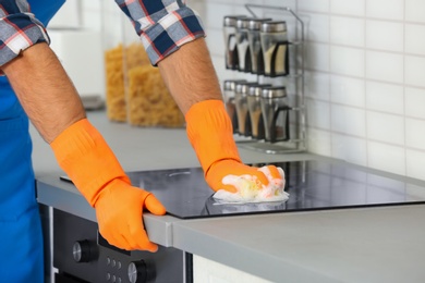 Photo of Man cleaning kitchen stove with sponge, closeup