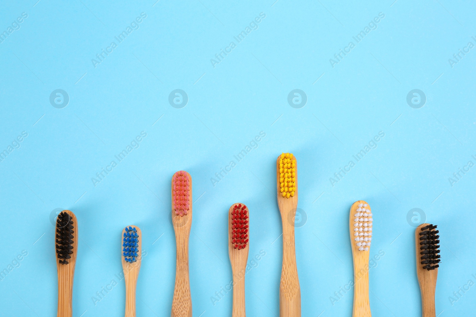 Photo of Toothbrushes made of bamboo on light blue background, flat lay. Space for text