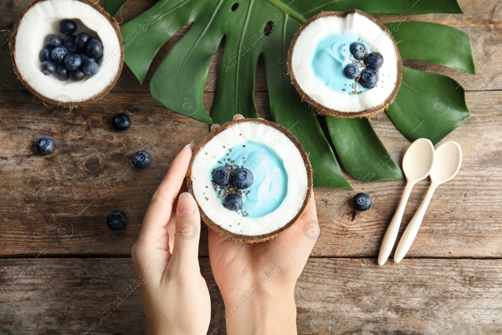 Photo of Woman holding coconut with spirulina smoothie on wooden table, top view