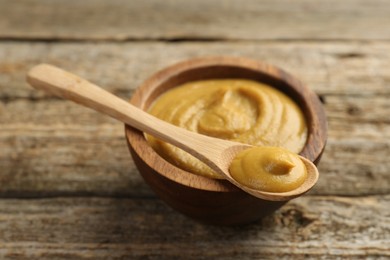 Photo of Spoon and bowl with tasty mustard sauce on wooden table, closeup