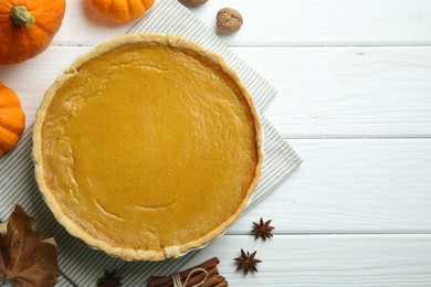 Delicious pumpkin pie and ingredients on white wooden table, flat lay. Space for text