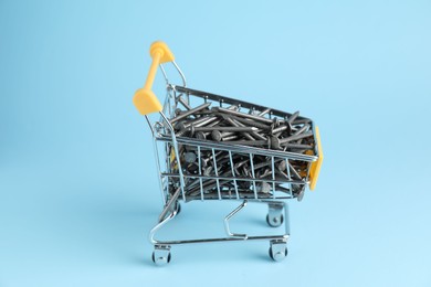 Photo of Metal nails in shopping cart on light blue background