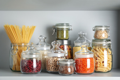 Photo of Glass jars with different types of groats and pasta on white shelf