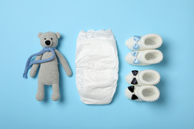 Photo of Diaper, toy bear and booties on light blue background, flat lay