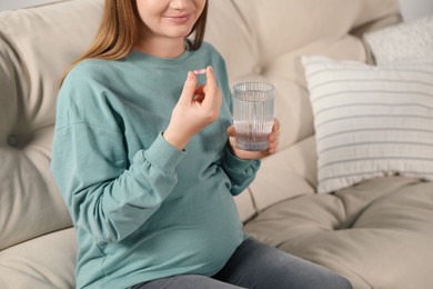 Photo of Pregnant woman holding pill and glass of water at home, closeup