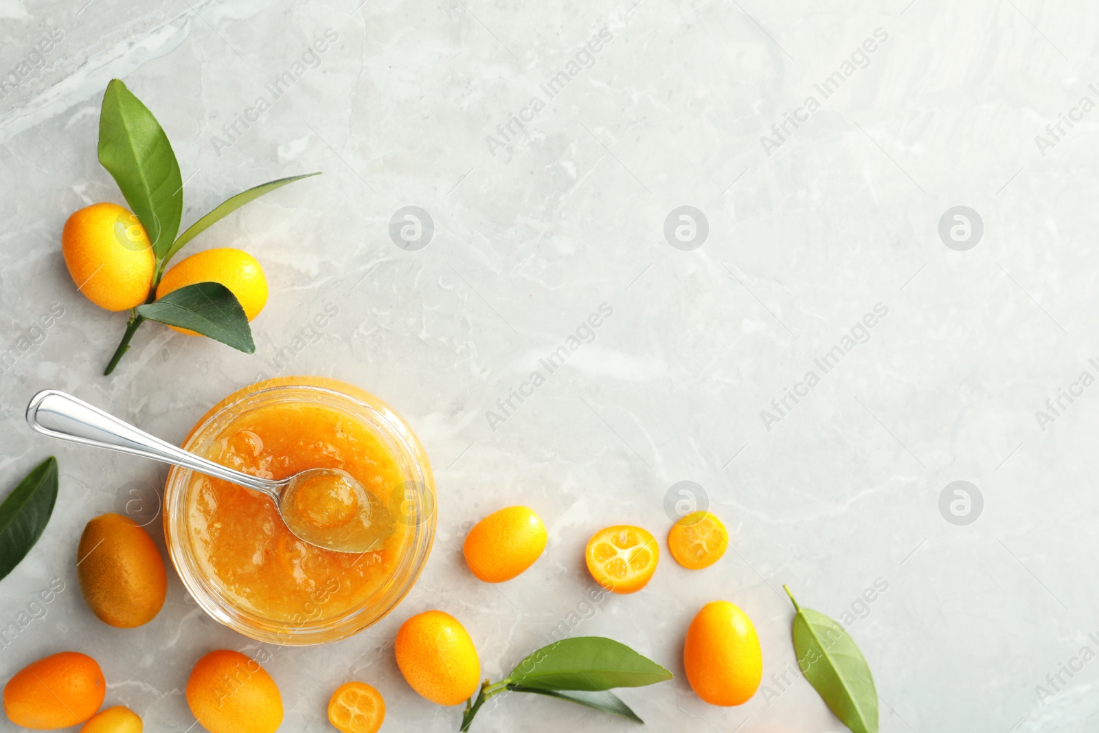 Photo of Delicious kumquat jam and fresh fruits on light grey marble table, flat lay. Space for text