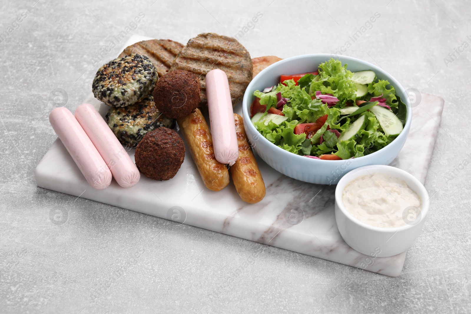 Photo of Different tasty vegan meat products, sauce and fresh vegetable salad on light grey table, closeup