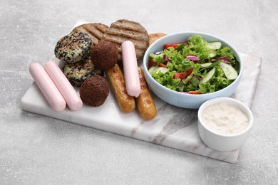 Photo of Different tasty vegan meat products, sauce and fresh vegetable salad on light grey table, closeup