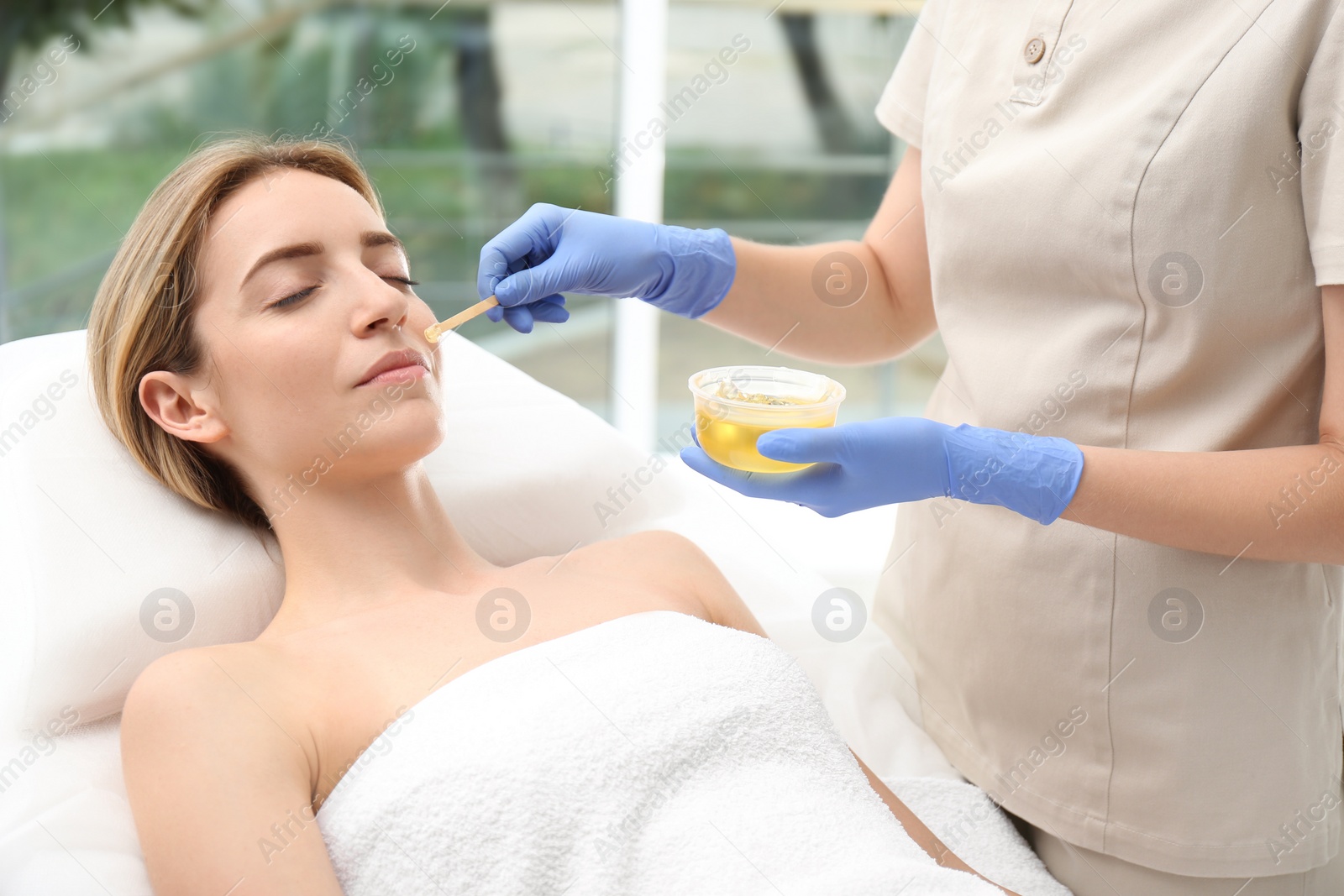 Photo of Beautiful woman getting wax epilation of face in salon