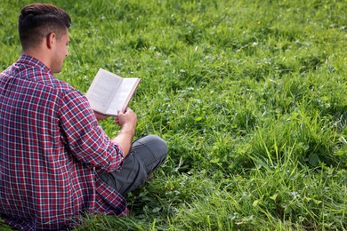 Photo of Man reading book on green grass, back view