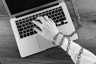 Top view of woman with chained hand using laptop at wooden table, black and white effect. Internet addiction