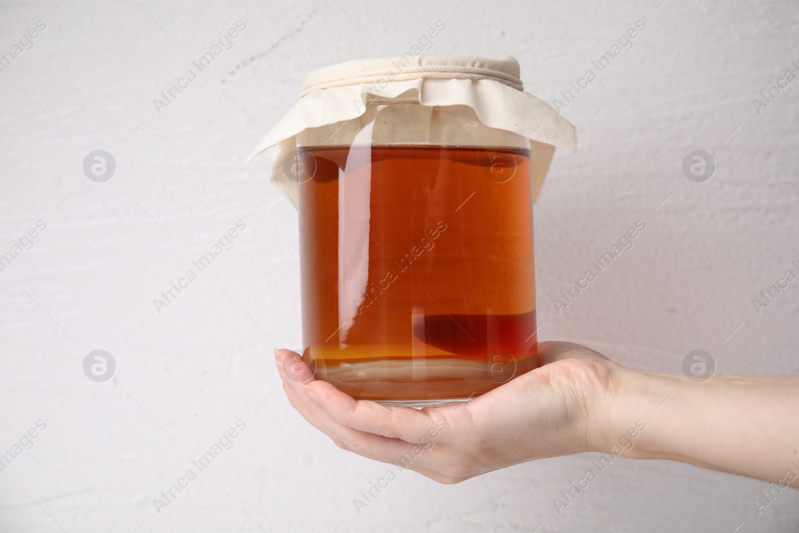 Photo of Woman holding glass jar of tasty kombucha on white background, closeup