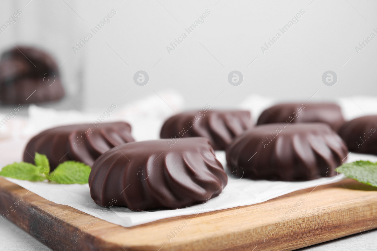 Photo of Delicious chocolate covered zephyrs and mint on wooden board, closeup