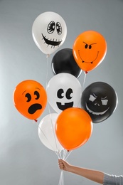 Woman holding color balloons for Halloween party on light grey background, closeup